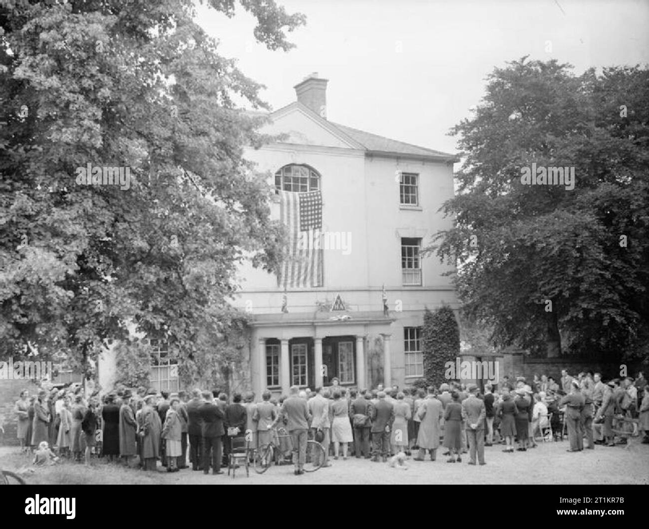 Amerikanische Botschaft Vertreter eröffnet neue Jugendherberge - Leben an Burgage Manor Jugendherberge, Southwell, Nottinghamshire, England, Großbritannien, 1944 eine allgemeine Ansicht der Eröffnung der Jugendherberge an Burgage Manor, Southwell. Sara Lamport der Amerikanischen Botschaft ist nur sichtbar in der Mitte. Eine große amerikanische Flagge wurde aus dem mittleren Fenster über dem Portal drapiert worden, und nur unterhalb dieser zwei kleine Union flags flankieren den YHA dreieckigen Logo auf dem Dach der Veranda. Viele Menschen drängen um, hören auf die Eröffnungsrede, darunter ein Mann mit einem Fahrrad. Ein Hund kann auch nur se Stockfoto