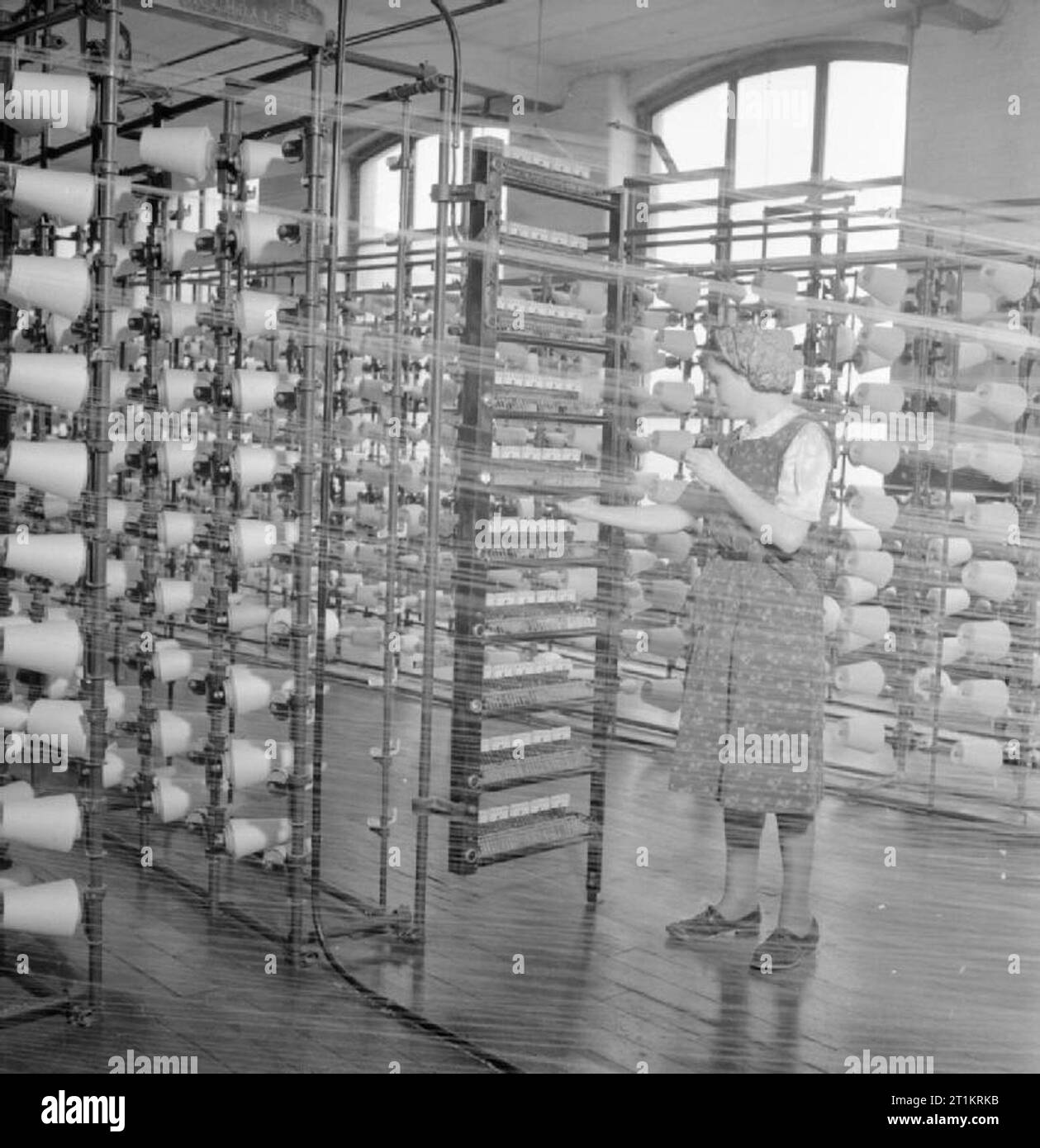 Der britischen Baumwollindustrie - Alltag an einer britischen Cotton Mill, Lancashire, England, Großbritannien, 1945 Hilda Mackenzie arbeitet als Ball warper in einer Baumwollspinnerei, irgendwo in Lancashire. Ihr Job ist die feinen Fäden auf einer kreisförmigen Holzbalken zu wickeln. Dieses Foto wird genommen durch die feinen Web von Threads. Zeilen und Zeilen der Rollen der Thread ist deutlich zu sehen. Stockfoto