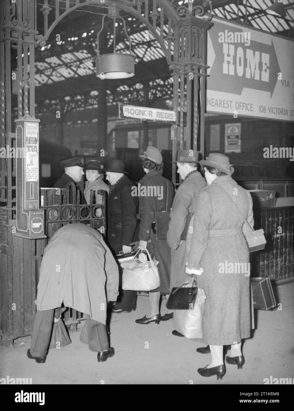 Die Fuhrleute in Kriegszeiten - Alltag für eine britische Familie auf dem Vorderen, England, C 1940 Frau Carter Warteschlangen zu Ihr Ticket am Tor zu einer Plattform, Victoria Station, London, auf dem Weg zu besuchen, ihre zwei Kinder, die Hayward Heath, Sussex evakuiert wurden. Beachten Sie die Gasmaske durch die Frau, die an der Rückseite der Warteschlange durchgeführt. Stockfoto