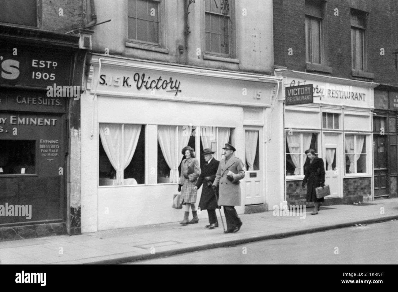 Der "Sieg" Restaurant in Soho, London, 1944. Ein Offizier in der Armee und mehrere Zivilisten Spaziergang, vorbei an einem Restaurant namens "Sieg" auf der Straße, im SOHO-Bereich von London. Die Legende besagt, dass das Wort "Sieg" erscheint in der ganzen Stadt und viele Cafés, Restaurants und andere Geschäfte haben' gestartet geben Sie uns Service', um das amerikanische Kontingent in Großbritannien, um sich wie zu Hause fühlen. Auf der linken Seite des Fotos, der Shop gerade sichtbar an der Ecke ist 'Lipman's", einem second-hand Kleidung kaufen. Die Straße, auf der dieses Foto aufgenommen wurde, schließt sich mit der griechischen Street in Soho. Stockfoto