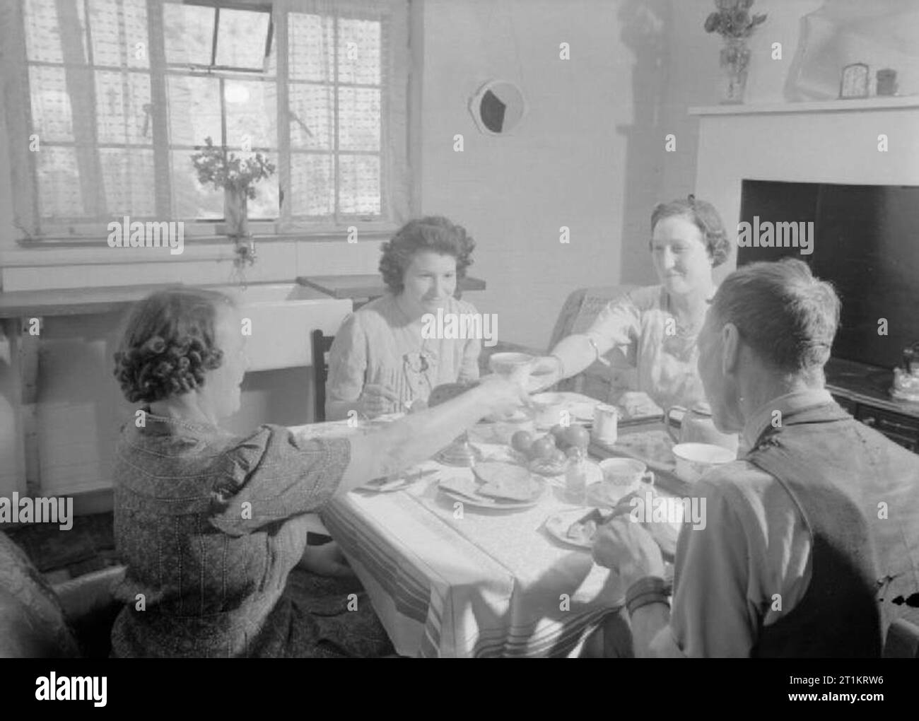 Die Cottages von Freefolk - Leben im Dorf Freefolk, Hampshire, England, UK, 1943 Die Shadwell Familie Kaffee in der Küche ihres Hauses im Freefolk, Hampshire genießt. Das Waschbecken können unter dem Fenster hinter ihnen gesehen werden, und einem großen Kamin dominiert der rechten Wand. Gemäß der ursprünglichen Beschriftung, es ist auch eine 'Groß' Speisekammer und eine Tür aus der Küche bietet Zugriff auf eine geflieste Terrasse, die zu Ihren Hinterhof. Stockfoto