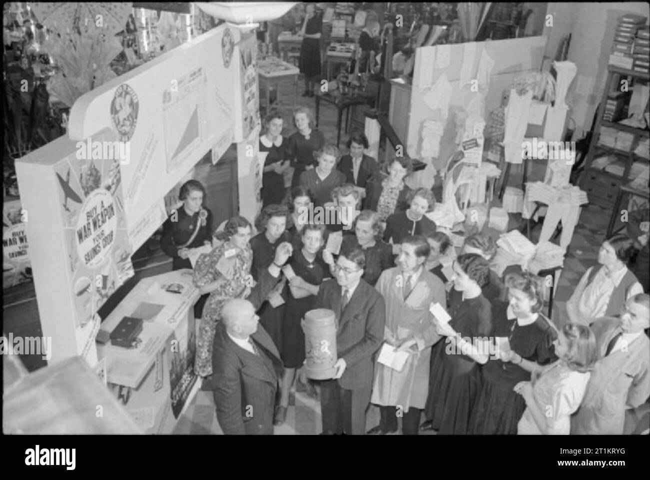 Die nationalen Ersparnisse Regelung bei der Arbeit in Canterbury, England, 1941 Mitarbeiter sammeln auf dem Shop floor von Lefevre, neben den Einsparungen, wie Bürgermeister Charles Lefevre, der auch der "Boss" der Gesellschaft, stellt die wöchentliche Ziehung unter den Mitarbeitern für eine kostenlose Einsparungen oder Bescheinigungen, die von der Verwaltung vorgelegt wird. Lefevre kann in der Mitte vorne gesehen werden, erhob seine Hand, bereit, in die "dip-Churn' wird von einem Helfer gehalten. Stockfoto