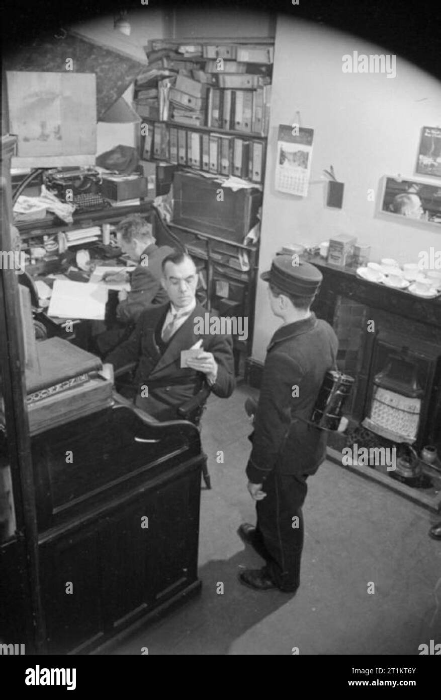 Das Telefon führt, London, Januar 1942 ein botenjunge liefert eine Nachricht an das Büro von einem Telefon Teilnehmer, dessen eigene Telefon system nach einem Luftangriff beschädigt wurde. Der Teilnehmer liest die Nachricht an seinen Schreibtisch, bevor Sie mit dem Messenger. Beachten Sie, dass der Bote seine Gasmaske trägt in ihrer Dose auf seinem Rücken und hat eine kleine Tasche für Nachrichten an der Vorderseite seiner Tunika. Stockfoto