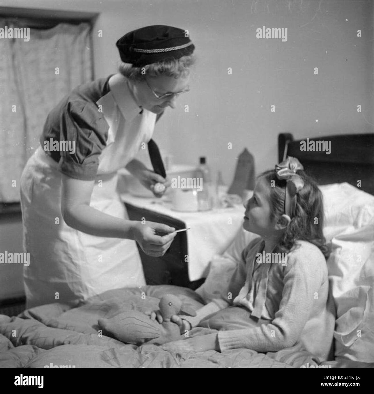 Ausbildung der Königin Krankenschwestern - Bezirk Krankenschwester Ausbildung im Queen's Institut für Bezirk Krankenpflege, Guildford, Surrey, England, Großbritannien, 1944 ein Traineeprogramm Bezirk Krankenschwester besucht die Heimat von einem jungen Mädchen, das sich nach einer Lungenentzündung. Das Mädchen ist im Bett sitzend und hält ein Tuch Spielzeug in der Form einer Ente. Stockfoto