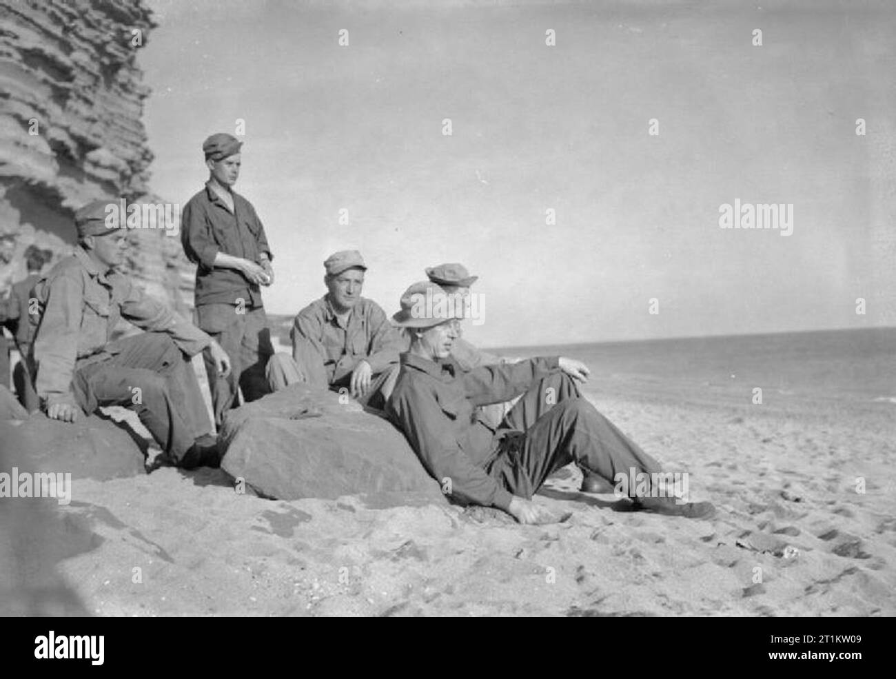 US-Truppen in einem englischen Dorf - den Alltag mit den Amerikanern im Burton Bradstock, Dorset, England, Großbritannien, 1944 eine Gruppe von amerikanischen Soldaten, die in die Sonne auf den Sand bei Burton Strand entspannen, südlich von Burton Bradstock in Dorset. Unter der Gruppe mit Blick auf das Meer sind: PFC-James Kran (von Harding, Missouri), privater Stanley T Miller (von Axtel, Kentucky), PFC W W Johnson (von Bluefield, West Virginia), T/5G R Miller (von 4106 Vermont Avenue, Louisville, Kentucky) und T/4 George Keister (von Fort Wayne, Texas). Die gezahnte Rock von Burton Cliff können hinter Ihnen auf der linken Seite der t gesehen werden. Stockfoto