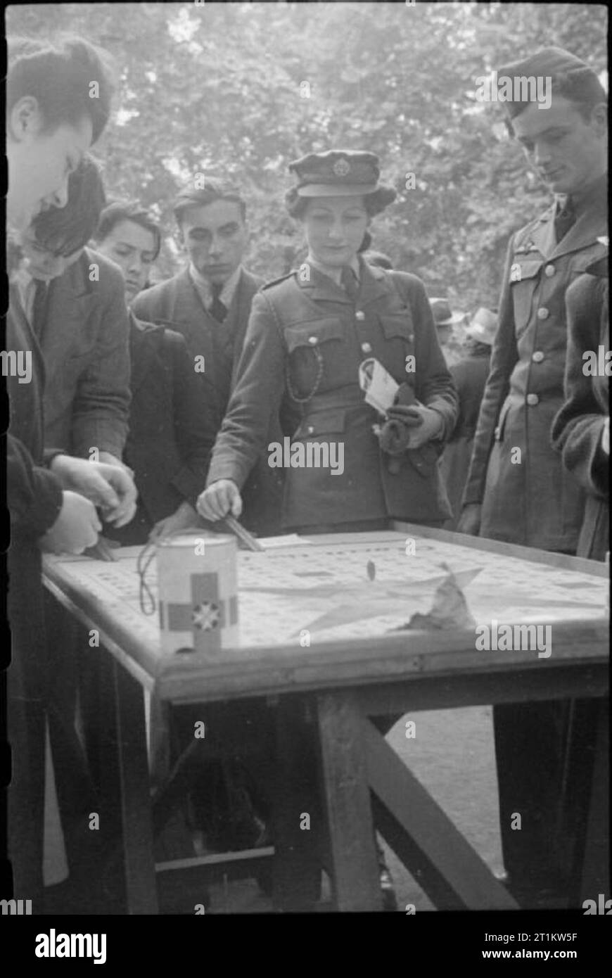 Krieg Fair - Urlaub zu Hause auf einer Fete in Russell Square, London, 1943 Mitglied der Women's Auxiliary Air Force spielt ein Spiel am Russell Square Fete. Ziel ist es, mit der WAAF einen Penny zu Rollen und erhalten es innerhalb der Linien eines bestimmten Platz zu landen, um die Zahlen im Quadrat markiert zu gewinnen. Unter den Zivilisten beobachtete sie wie sie spielt, ist ein amerikanischer Pilot, das Tragen von RAF-Flügel. Gemäß der ursprünglichen CAPTION,'seine doppelte Flügel bedeutete, dass er einmal für Großbritannien geflogen': Wäre er Mitglied einer Eagle Squadron. Stockfoto