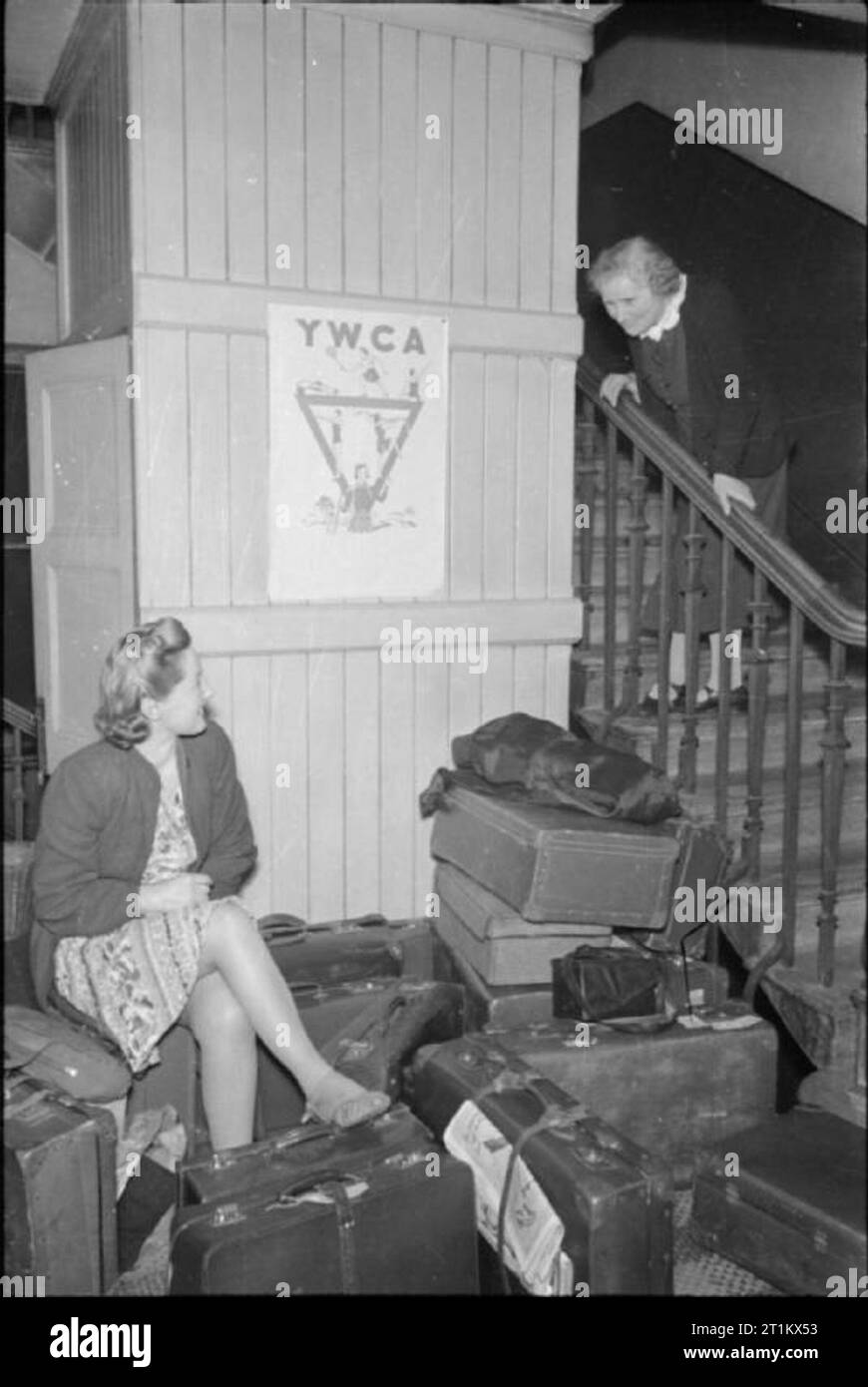 Ein Mädchen schließt sich - Women's Factory, England, UK, Mai 1941 Vera Elliott sitzt auf einem Haufen von Koffern in der Eingangshalle des YWCA Rezeption Hostel, wo Sie und Ihre Kollegen neue Rekruten die Nacht verbringen werden. Sie ist von Miss Smart, die Matrone, die schiefen ist über das Geländer zu Vera zu sprechen, begrüßt. Miss Smart läuft das Hostel mit ihrer Schwester. Stockfoto