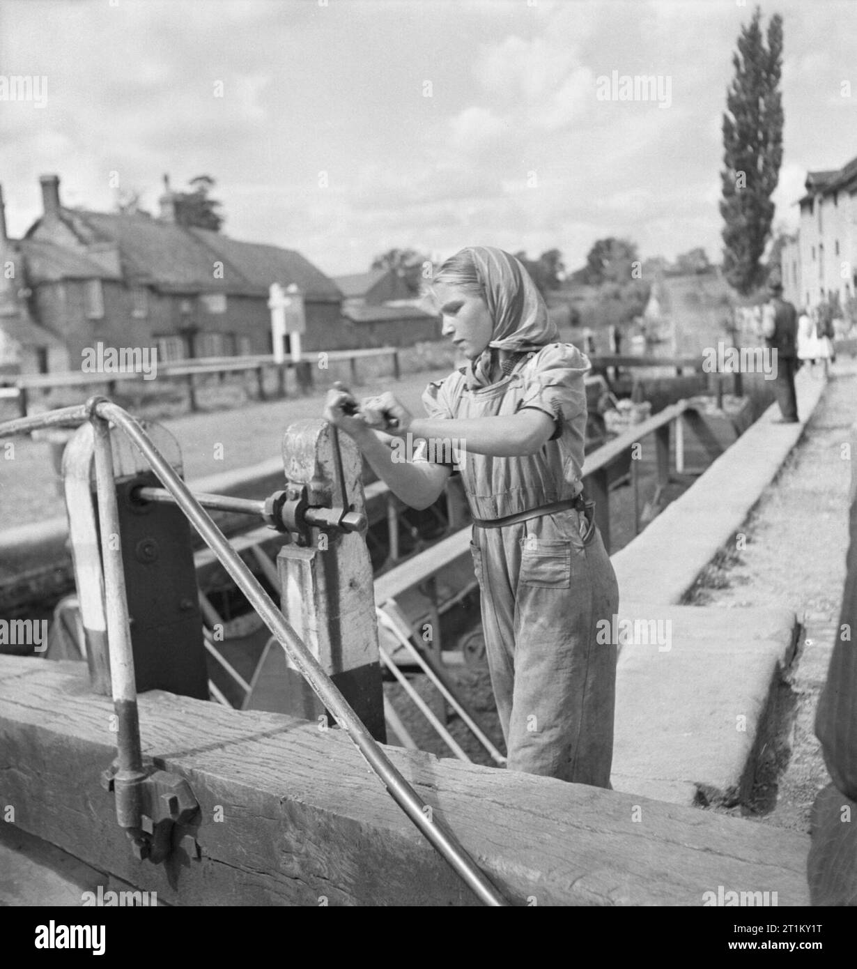 Britische Kanäle in Kriegszeiten - Verkehr in Großbritannien, 1944 ein junges Mädchen, Tochter eines Kanals Boatman, dreht sich der Griff einer Sperre, irgendwo entlang der Grand Union Canal. Sie ist Liquidation die Paddel das Wasser aus der obersten Ebene füllen Sie die Sperren zu lassen und die Boote heben. Die Ursprüngliche Bildunterschrift heißt es, dass "jedes Mal, wenn ein paar Boote geht nach oben oder unten, verwenden Sie eine Sperre von Wasser (5.600 Gallonen). Wasser wird durch das Senden Boote durch abwechselnd in entgegengesetzte Richtungen gespeichert. Wenn ein paar Boote hat gerade gegangen, die Sperre ist voll für ein Paar "Absteigend". Stockfoto