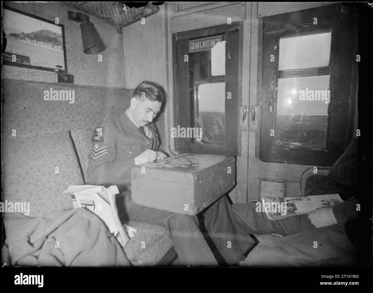 British Railways in Kriegszeiten - Verlassen der Bahn - Verkehr zwischen London und Schottland, Großbritannien, 1944 In einem Raucherzimmer Fach auf einer Bahn zwischen London und Schottland, ein Royal Air Force Flight Sergeant niederlässt, um ein Puzzle der Zeit auf der Reise zu führen. Er ist mit seinen Fall als Tabelle, auf die sich die Puzzleteile zu verbreiten. Stockfoto
