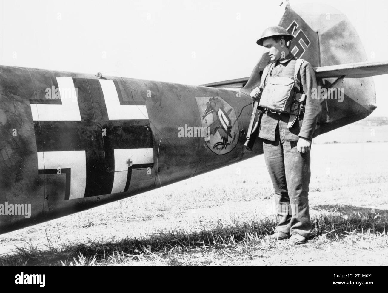 Die Schlacht von Großbritannien Mitglied der Home Guard steht durch den hinteren Rumpf der Messerschmitt Bf 109 E-4 (W.Nr. 5587) "Gelb 10" vom 6./JG 51 "Ältesten", die Crash-im East Langdon in Kent, 24. August 1940 landete. Der Pilot, Oberfeldwebel Beeck, blieb unverletzt eingefangen. Beachten Sie die II Gruppe Emblem eines weinenden Vogel mit einem Regenschirm unter ihre Fittiche und die Inschrift "Gott bombardieren England' versteckt. Stockfoto