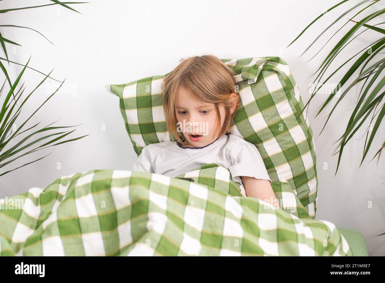 Bettenverrottung. Mit seinem Tablet in der Hand sitzt der junge Junge bequem auf dem Bett und erkundet in seinem Tempo das Internet Stockfoto