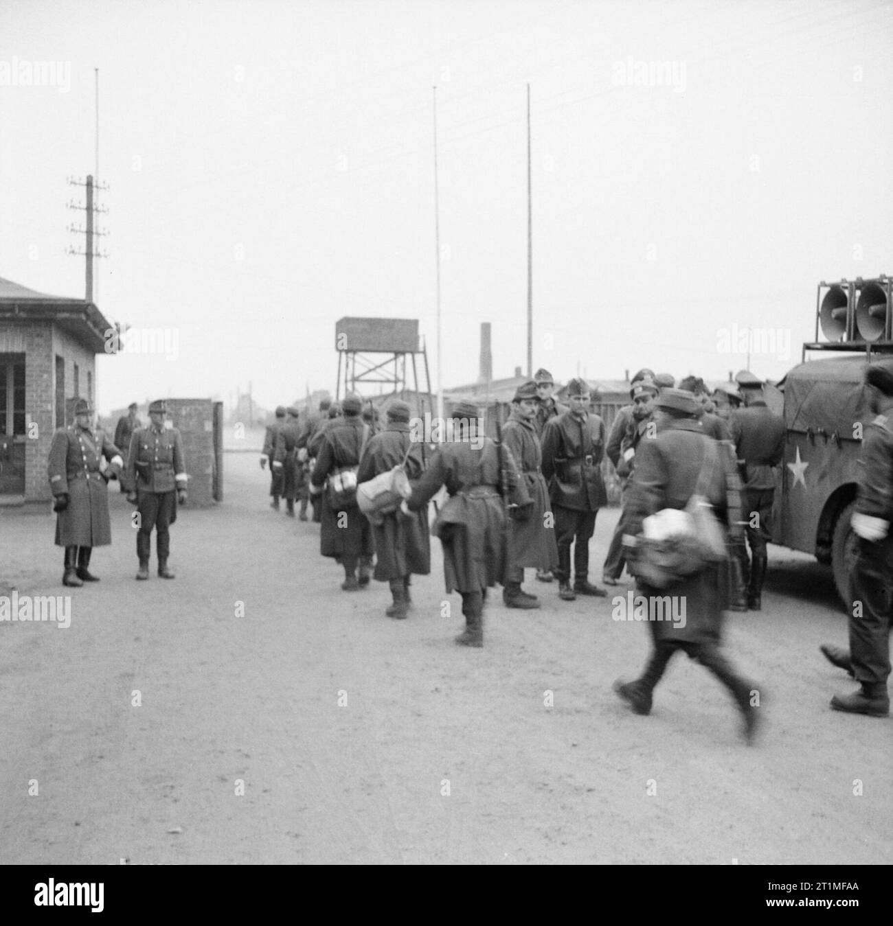 Die Befreiung des Konzentrationslagers Bergen-belsen, April 1945 die britische Armee kommt im Konzentrationslager Belsen an. Deutsche und ungarische Wachen stehen am Lagereingang, als deutsche Wehrmachtseinheiten (mit weißen Armbändern) im Rahmen des Waffenstillstandsabkommens mit den Briten vom 12. April 1945 in das Lager einmarschieren. Rechts ist ein Fahrzeug mit Lautsprechern der 14 Amplifier Unit, Intelligence Corps unter dem Kommando von LT Derrick Sington (Q103469181). Dieses Fahrzeug, begleitet von Fahrzeugen des 63. Anti Tank Regiment, Royal Artillery, war das erste, das das Lager betreten und wurde verwendet, um die zu informieren Stockfoto