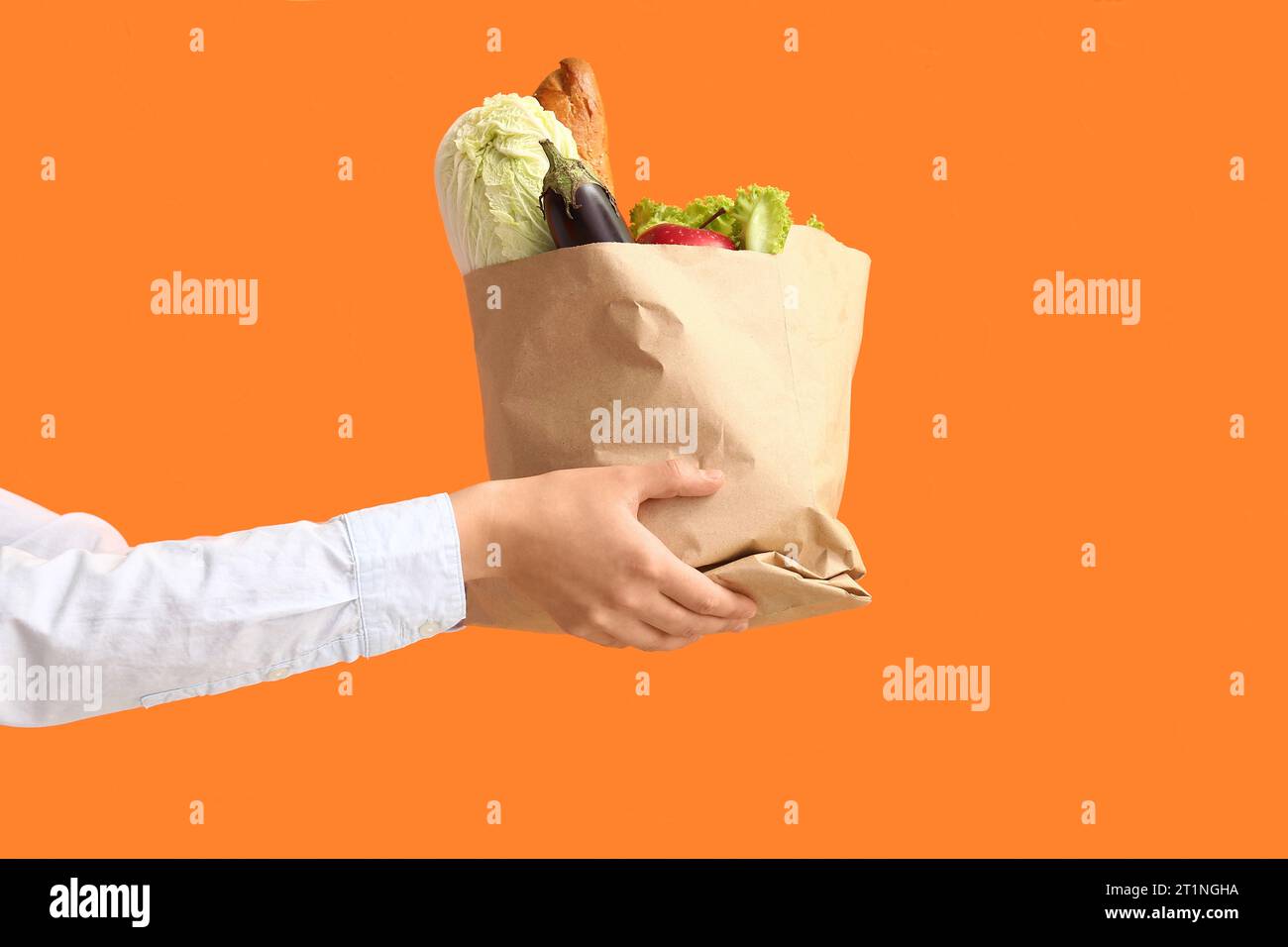 Frau, die Papiertüte mit frischem Essen auf orangem Hintergrund hält Stockfoto