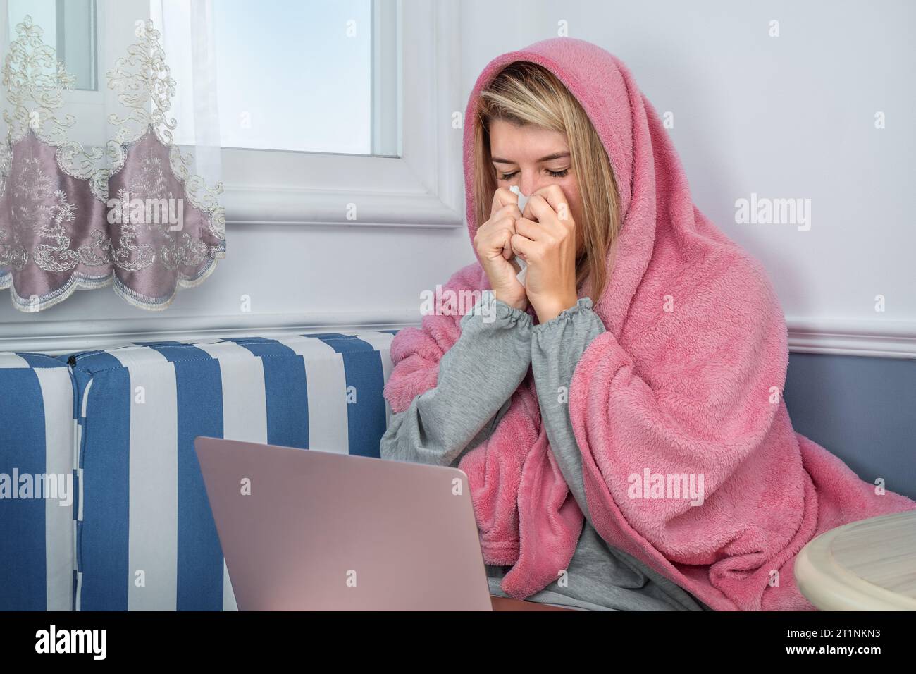 Ein Mädchen niest in einer Decke und benutzt zu Hause einen Laptop Stockfoto