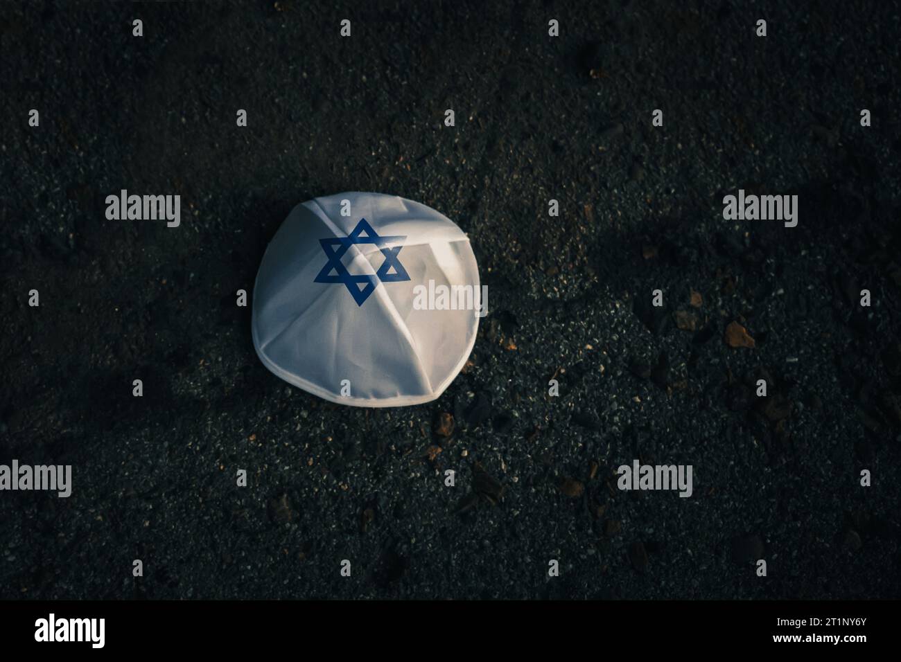 Gestrickte Kippahmütze im Stil der israelischen Flagge auf dunklem Asphaltgrund Stockfoto