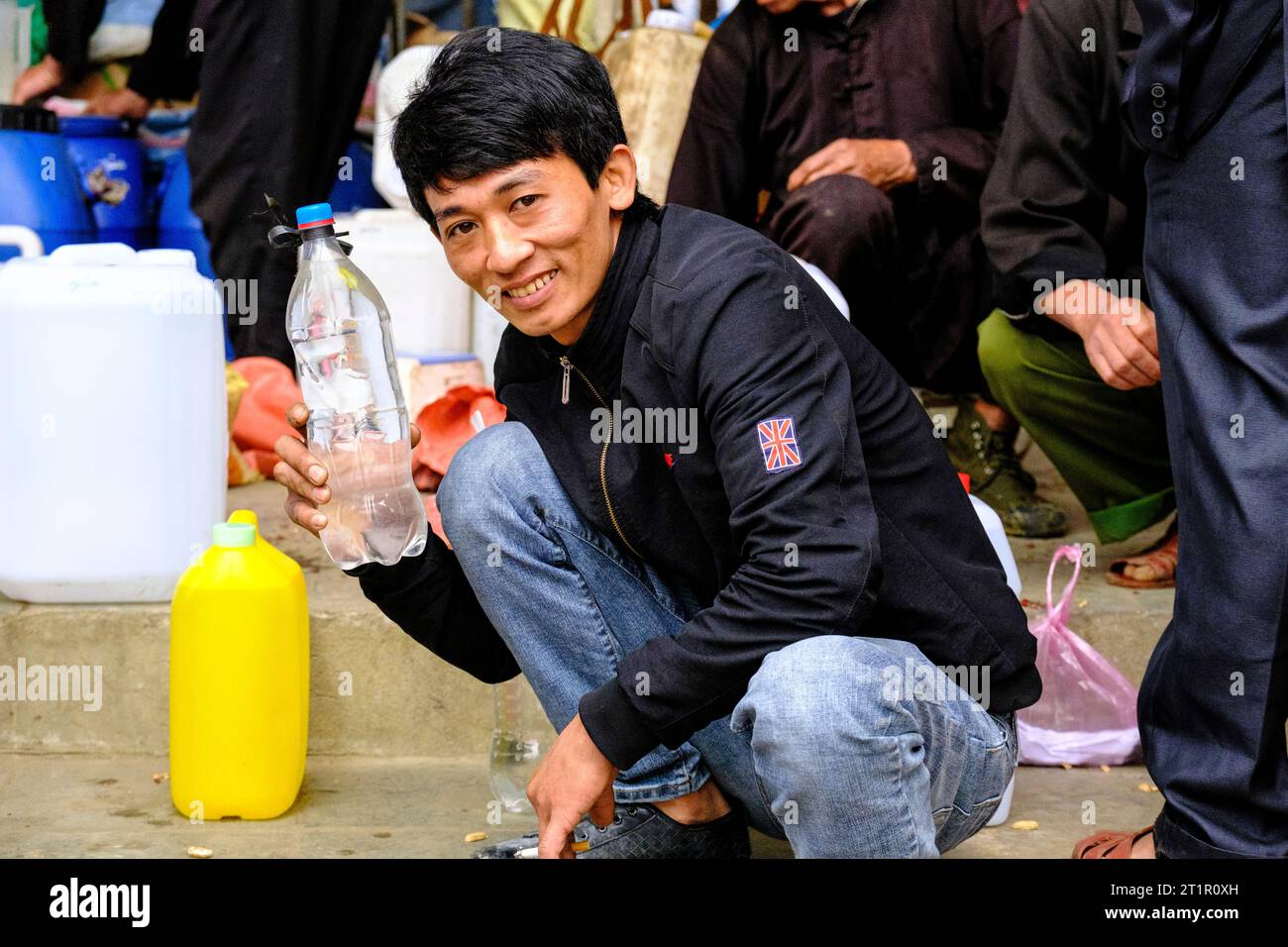 Bac Ha, Vietnam. Sonntagsszene. Junger Mann bietet hausgemachte alkoholische Getränke zum Verkauf an. Provinz Lao Cai. Stockfoto