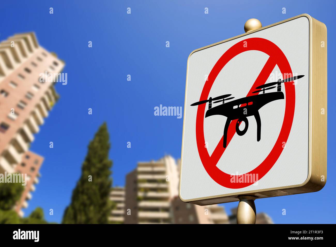 Drohnen-Verbotsschild (Straßenschild für das Gebiet der Flugdrohnen) vor einem klaren blauen Himmel in einer Stadt mit verschwommenen Wohngebäuden, Fotografie. Stockfoto