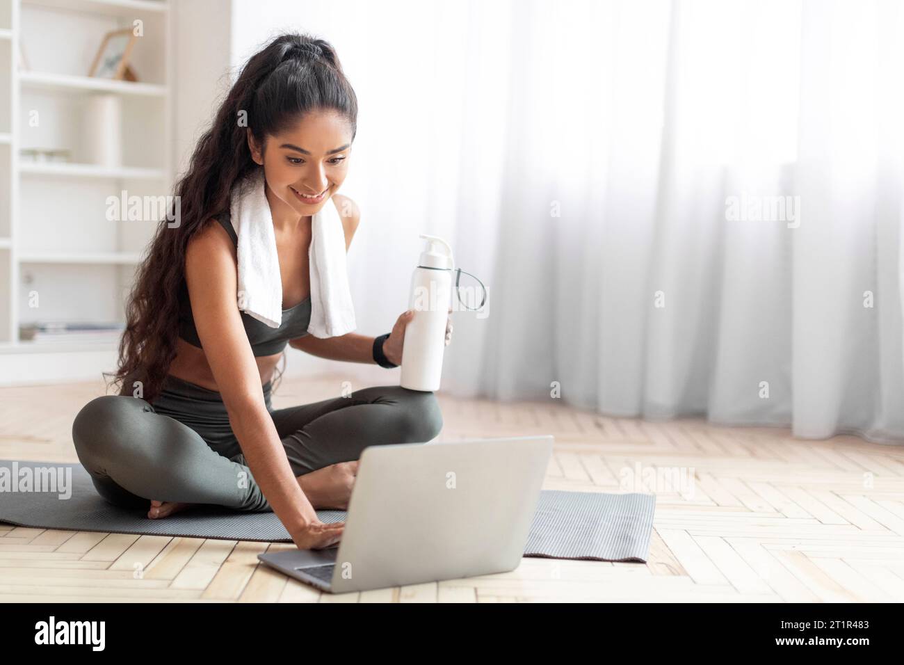 Glückliche indianerin, die eine Pause vom virtuellen Workout macht und Wasser trinkt Stockfoto