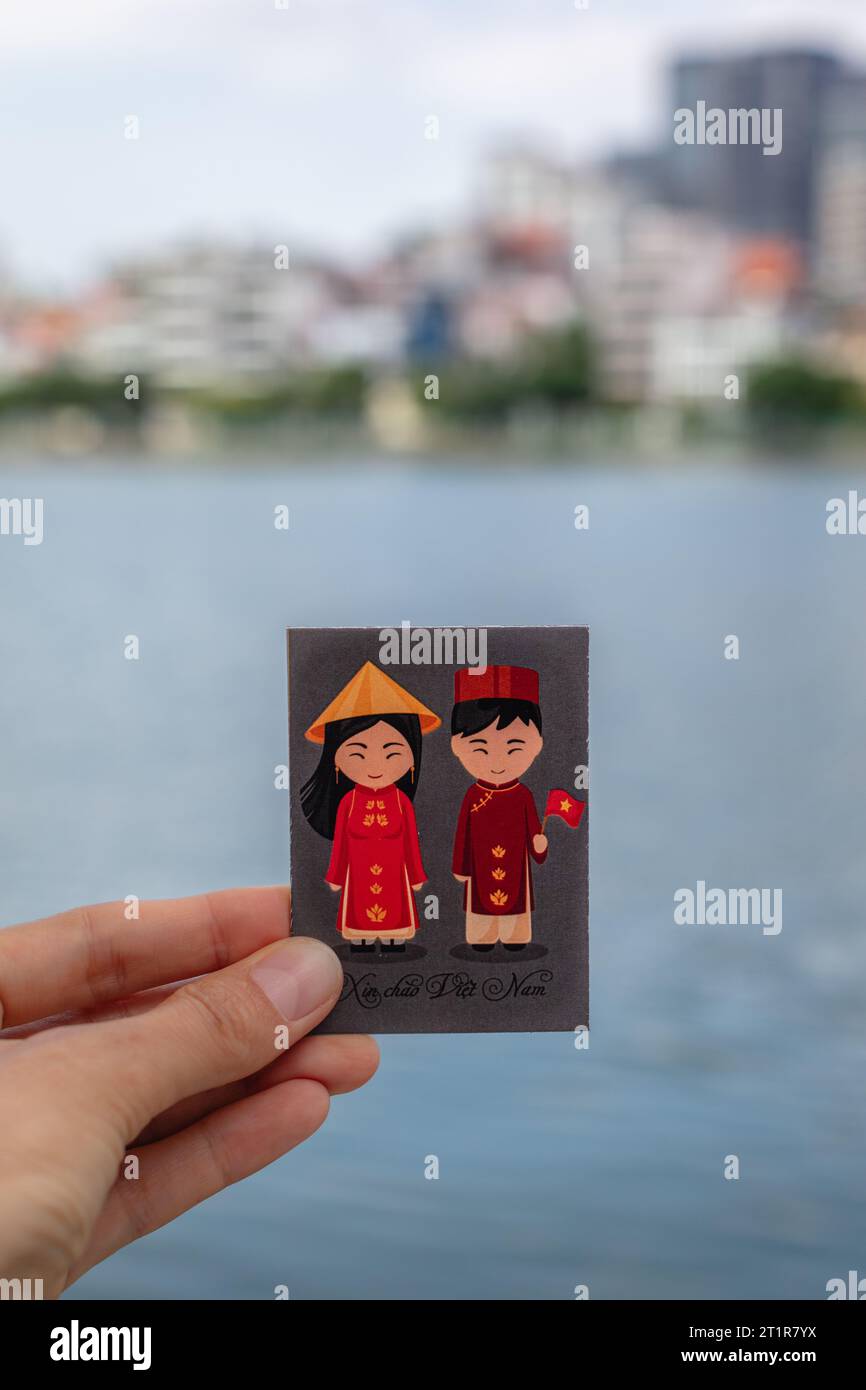 Magnet mit vietnamesischem Mädchen und Jungen in traditionellen Outfits. Im Hintergrund Quan Tay Ho oder Westlake District in Hanoi, Vietnam. Stockfoto