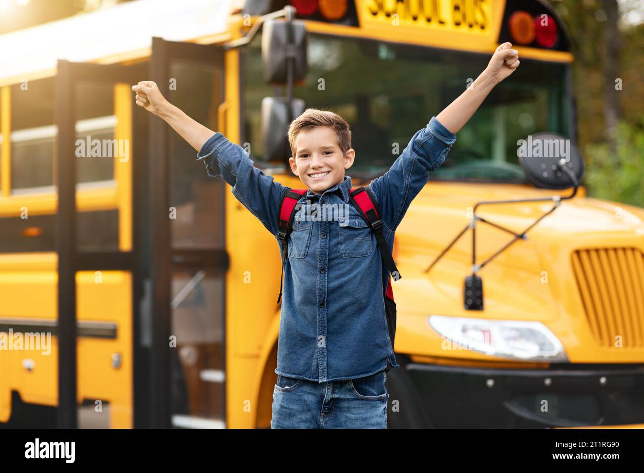 Glücklich Aufgeregt, Junger Junge, Der Arme Hebt, Während Er In Der Nähe Des Gelben Schulbusses Steht Stockfoto
