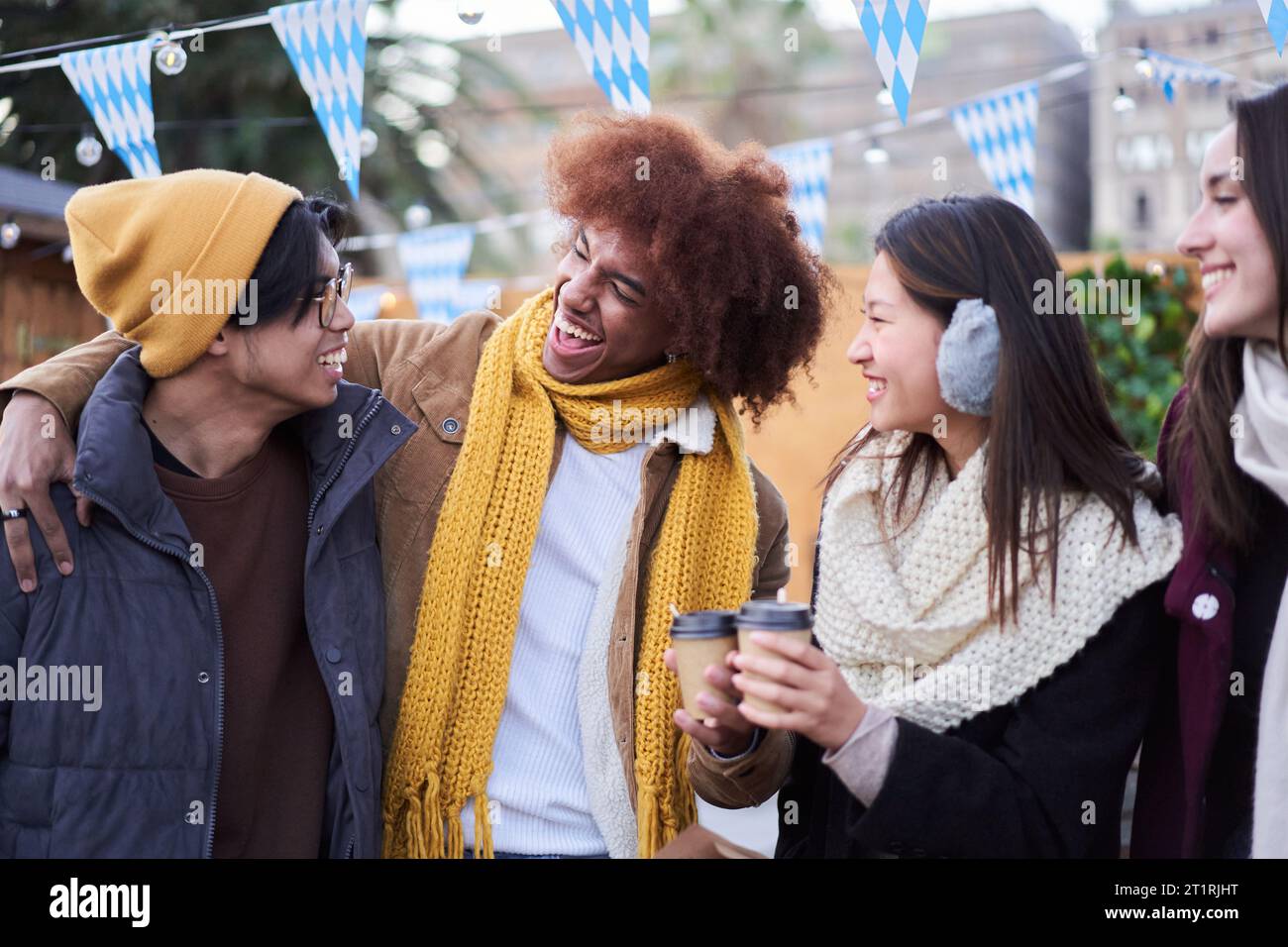 Lachende Freunde trinken zusammen heiße Getränke auf der Straße draußen. Generation z fröhliche Gruppenmenschen. Stockfoto