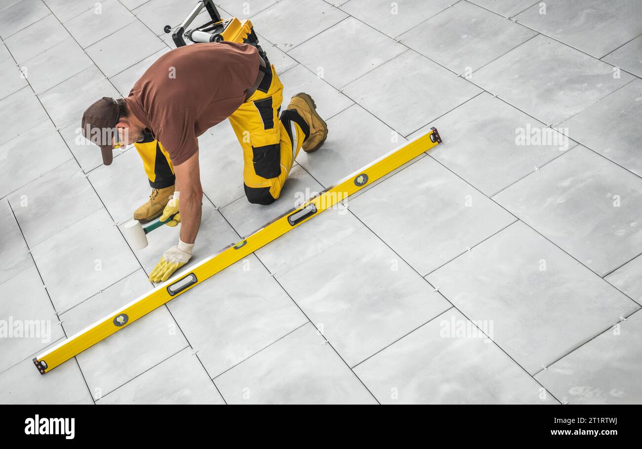 Kaukasischer Bauarbeiter Gebäude Terrasse Betonboden. Feinschliff mit einem weichen Hammer Stockfoto