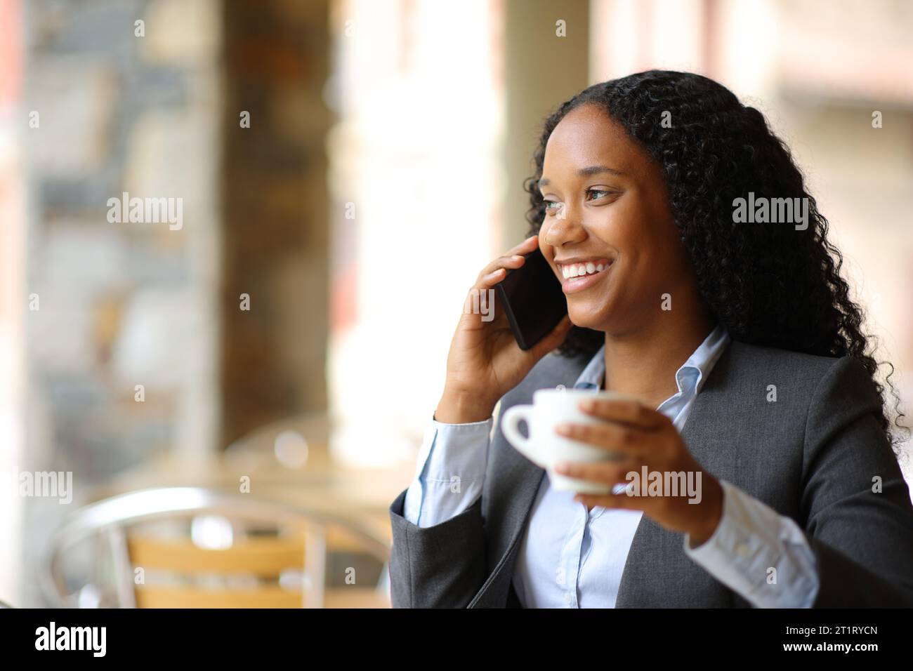 Glücklicher schwarzer Manager, der am Telefon sitzt und auf einer Restaurantterrasse sitzt Stockfoto