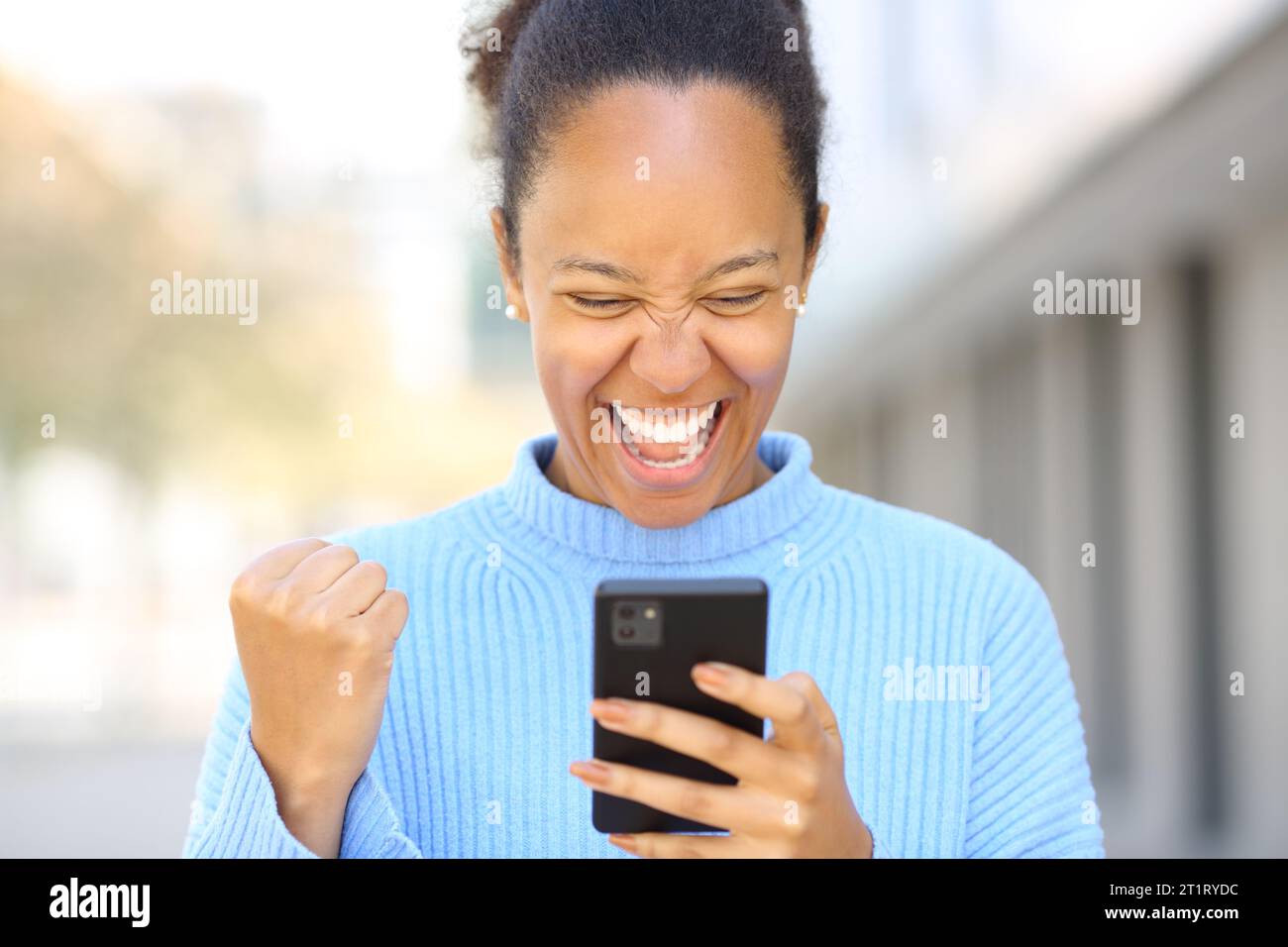 Vorderansicht Porträt einer aufgeregten schwarzen Frau, die auf der Straße gute Nachrichten am Telefon überprüft Stockfoto