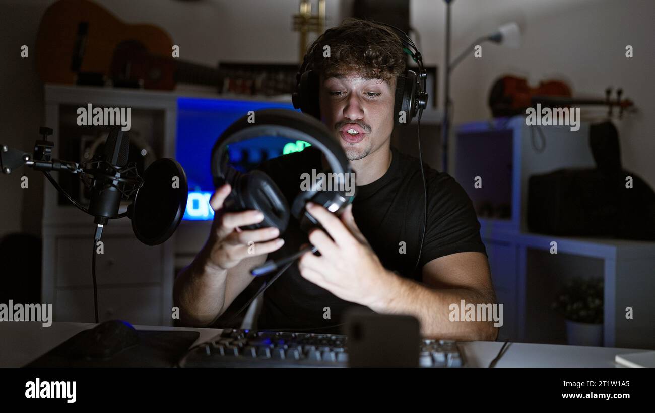 Gutaussehender hispanischer Mann, gefangen in aufregenden nächtlichen Gaming-Streams, vertieft in virtuelle Gespräche im Glanz seines Spielraums, Kopfhörer r Stockfoto