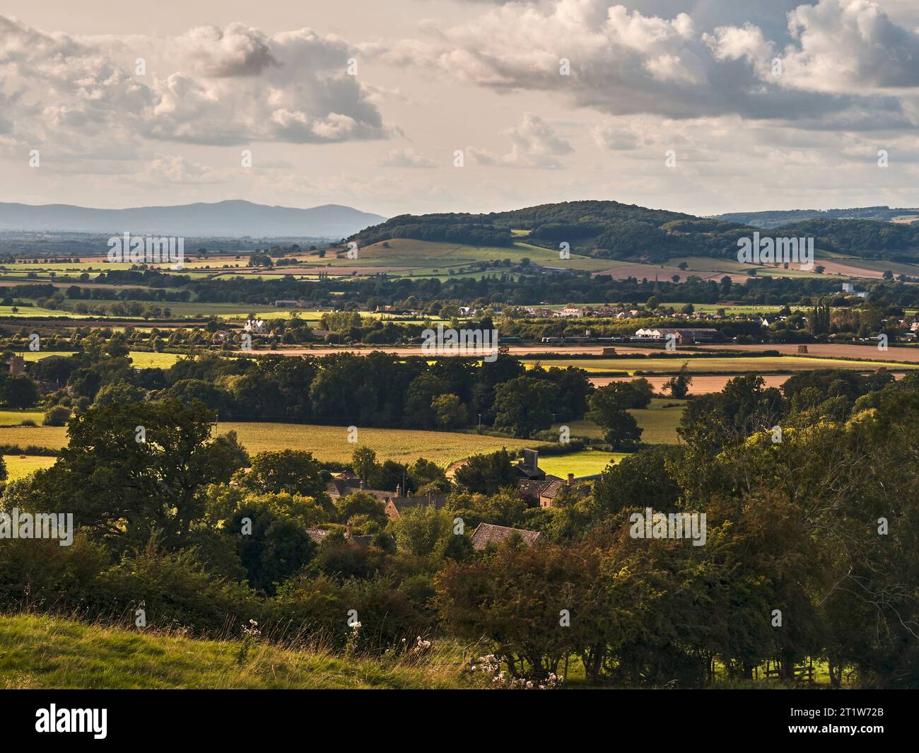 Blick auf das kleine Dorf Wood Stanway im Vordergrund, New Town, Dumbleton Hill und die Malvern Hills in der Ferne. Stockfoto