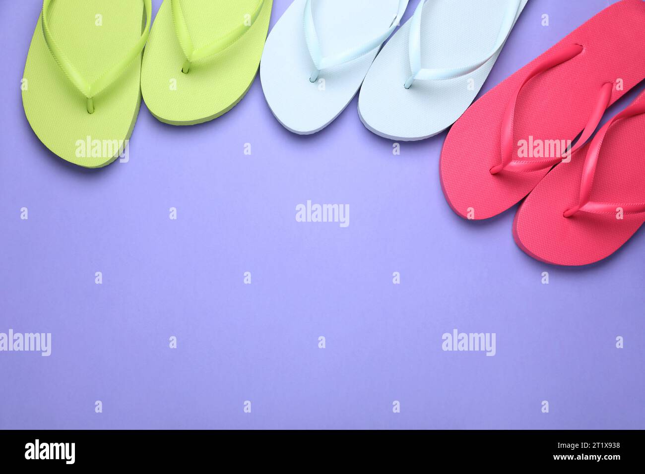 Viele verschiedene Flipflops auf hellviolettem Hintergrund, flach gelegt. Leerzeichen für Text Stockfoto