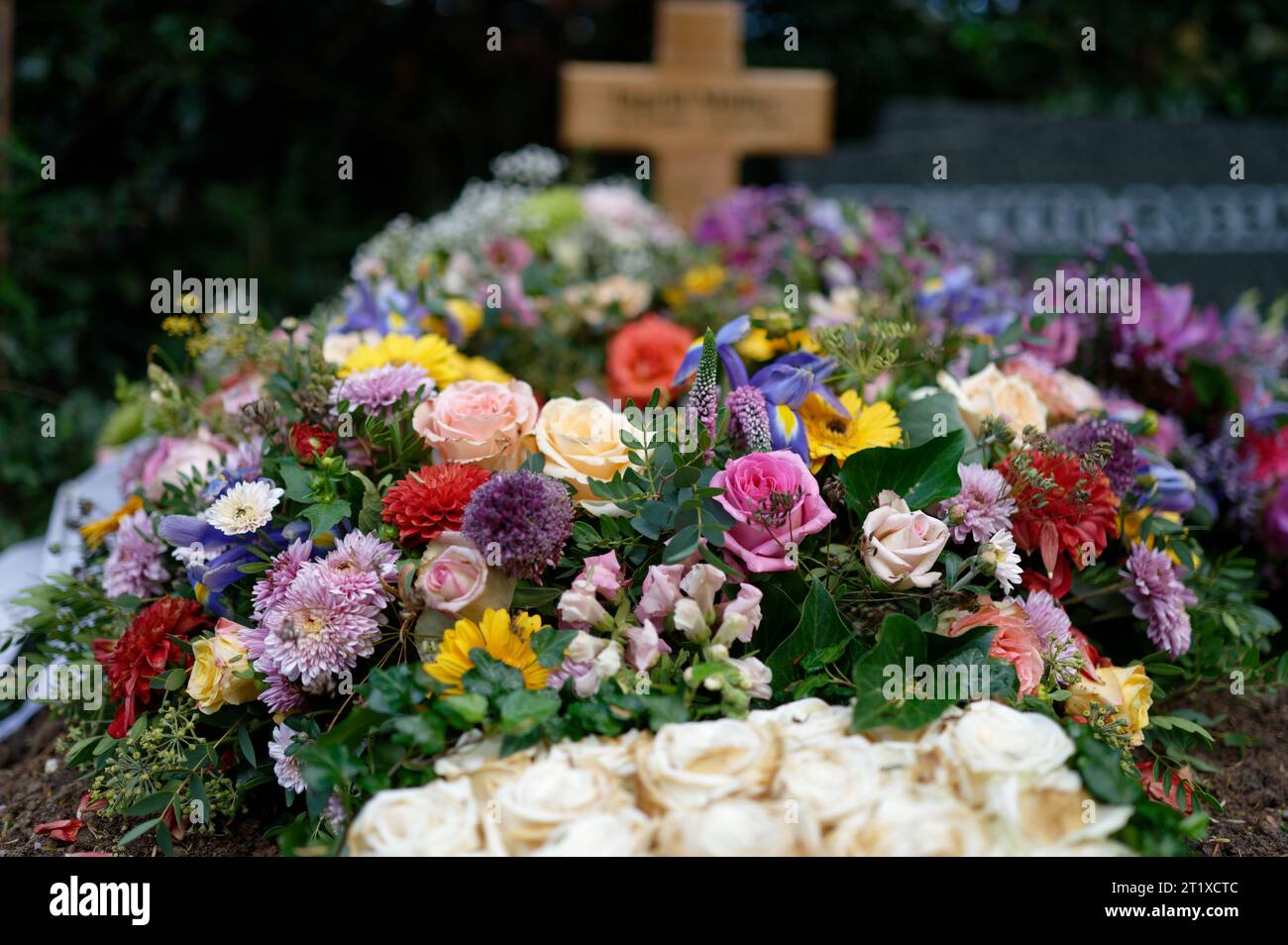 Trauerkranz auf einem Grab mit bunten Blumen und einem Holzkreuz in einem verschwommenen Hintergrund Stockfoto