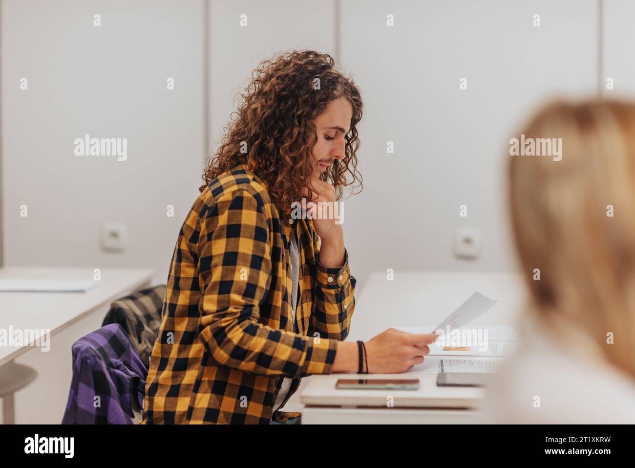 Seitenfoto eines langhaarigen männlichen Mitarbeiters, der Prüfungsfragen liest Stockfoto