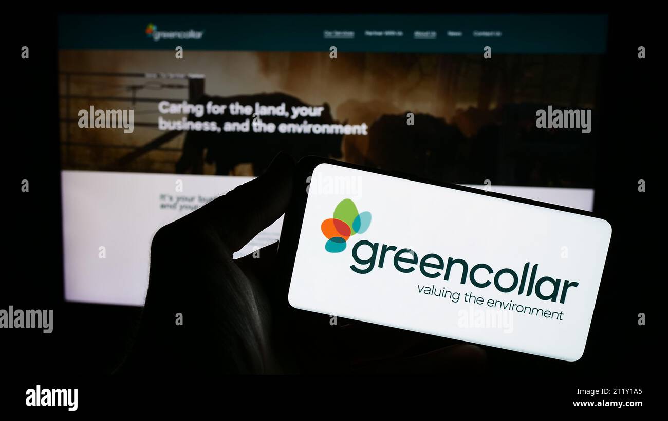 Person mit Smartphone und Logo der australischen Investmentgesellschaft GreenCollar Group vor der Website. Schwerpunkt auf dem Display des Telefons. Stockfoto