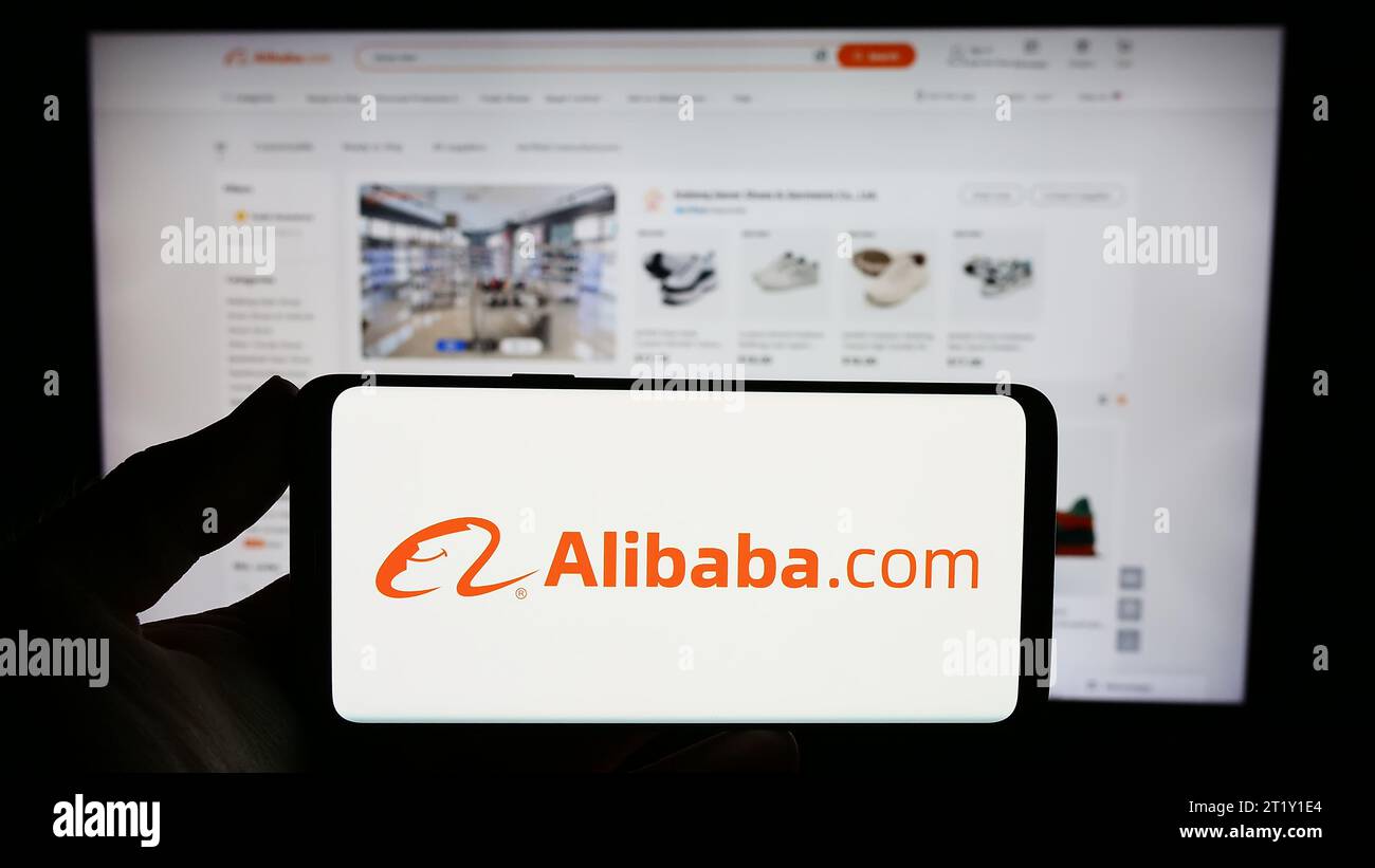 Person mit Smartphone und Logo der chinesischen B2B-E-Commerce-Plattform Alibaba.com vor der Website. Schwerpunkt auf dem Display des Telefons. Stockfoto