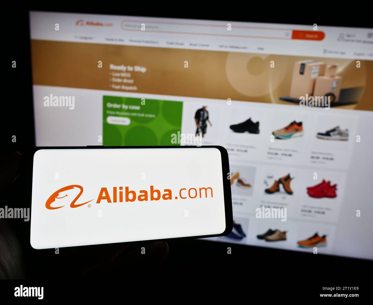 Person, die ein Mobiltelefon mit dem Logo der chinesischen B2B-E-Commerce-Plattform Alibaba.com vor der Business-Webseite hält. Schwerpunkt auf dem Display des Telefons. Stockfoto