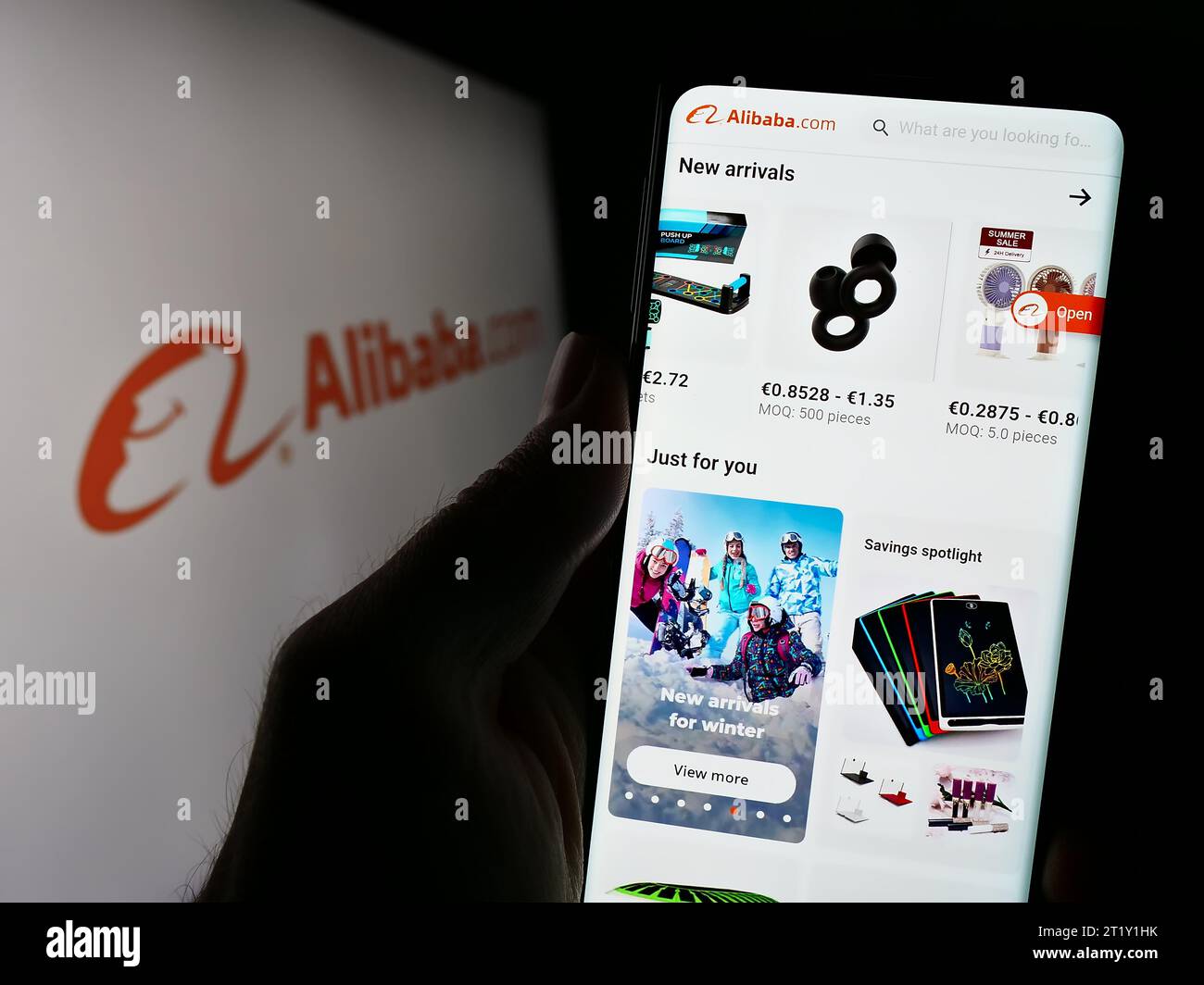 Person mit Smartphone und Website der chinesischen B2B-E-Commerce-Plattform Alibaba.com vor dem Logo. Konzentrieren Sie sich auf die Mitte des Telefondisplays. Stockfoto