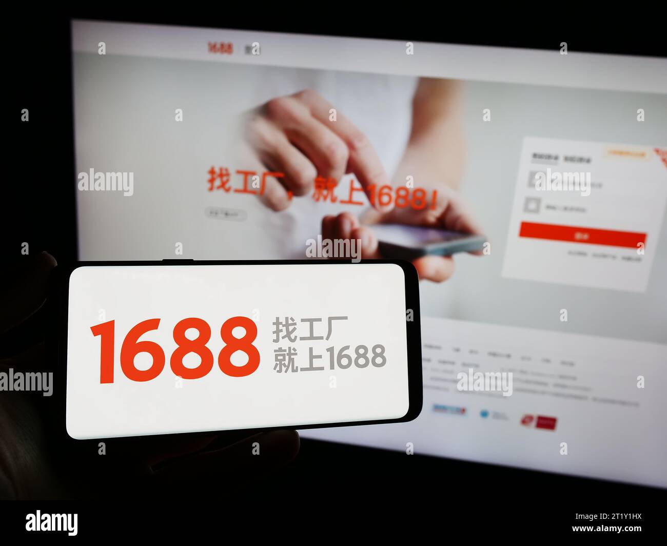 Person mit Smartphone und Logo des chinesischen Online-Shops 1688.com (Alibaba) vor der Website. Schwerpunkt auf dem Display des Telefons. Stockfoto
