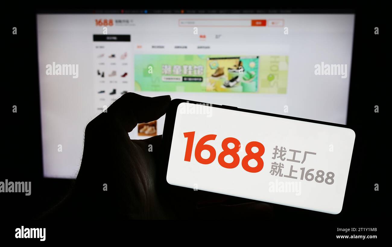 Person, die ein Mobiltelefon mit dem Logo des chinesischen Online-Shops 1688.com (Alibaba) vor der Business-Website hält. Schwerpunkt auf dem Display des Telefons. Stockfoto