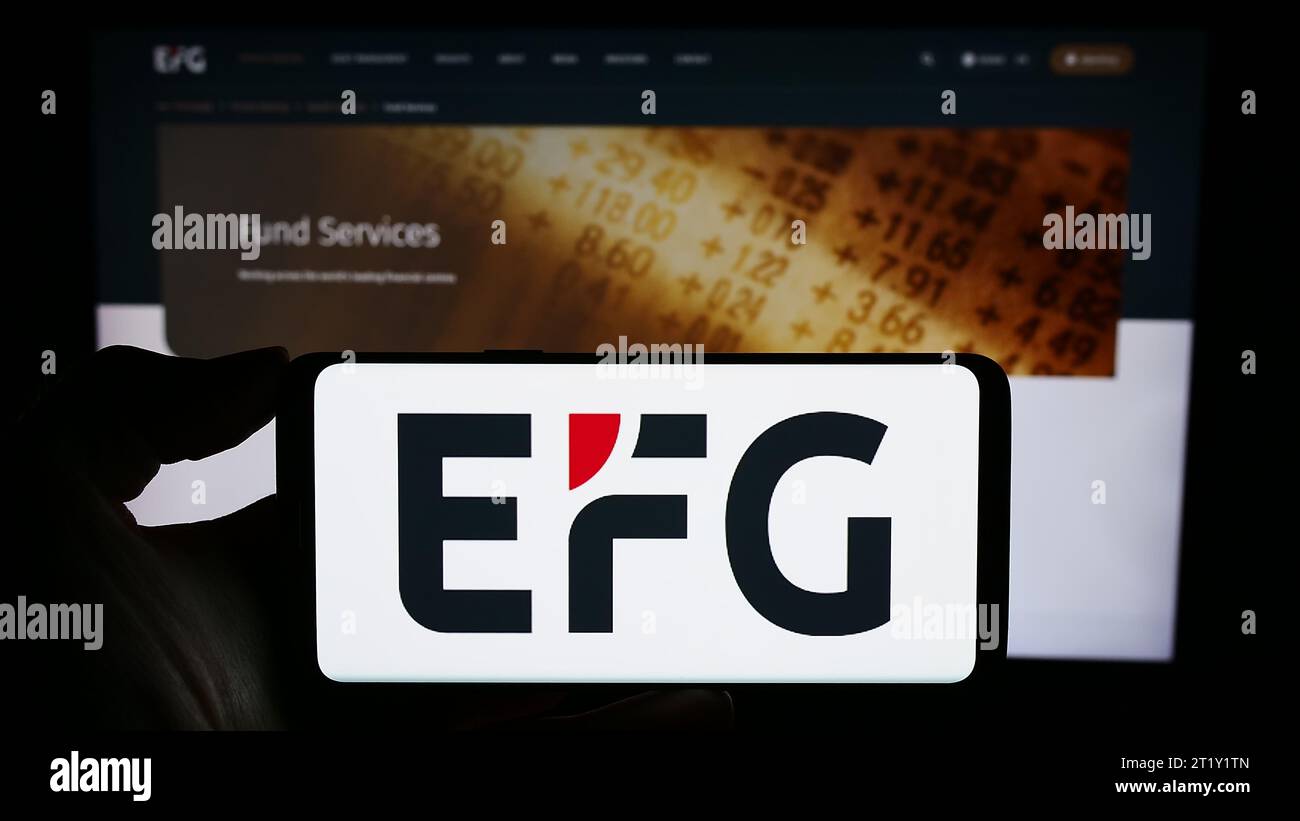 Person mit Mobiltelefon mit Logo der Schweizer Privatbank EFG International AG vor der Business-Webseite. Schwerpunkt auf dem Display des Telefons. Stockfoto