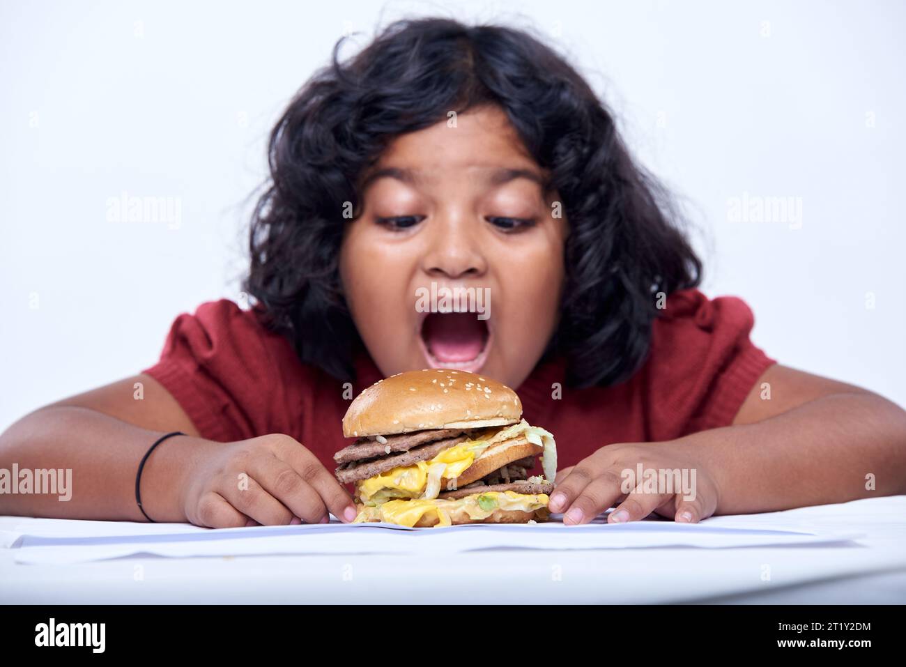 Ein glückliches lächelndes Mädchen isst gleich einen Hamburger. Fastfood auf weißem Hintergrund Stockfoto