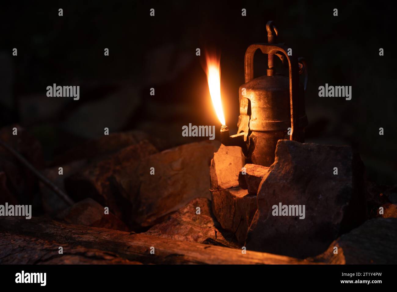 Brennende alte Karbidlampe mit hoher Flamme, die zwischen kleinen Quarzitsteinen steht. Dunkle Nacht, natürliche Szene, flacher Fokus. Stockfoto