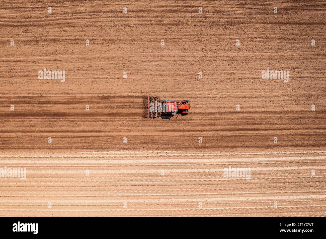 Roter landwirtschaftlicher Traktor mit angebauter Deichsel, der vor der Aussaat die Bodenbearbeitung durchführt, Luftaufnahme vom Drohnen-pov von oben nach unten Stockfoto