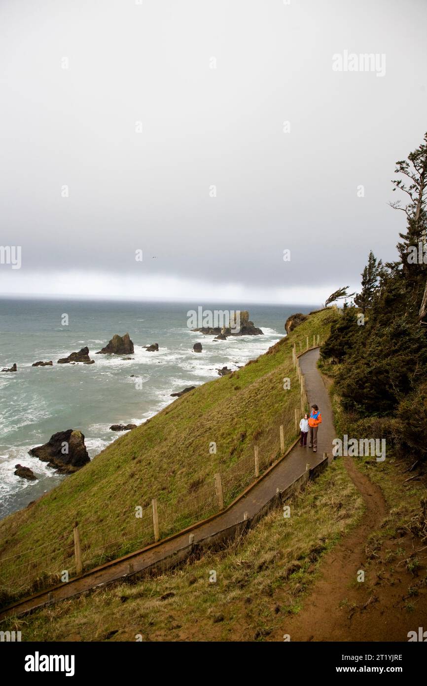 Besucher genießen einen gepflasterten Pfad mit Blick auf die stürzenden Wellen am Rande der steilen Küste von Oregon. Stockfoto