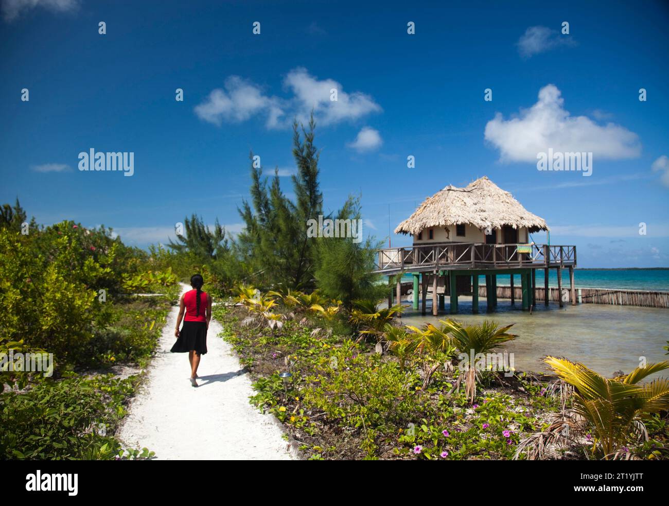 Eine Frau läuft einen kleinen Weg in der Nähe von strohbedeckten Räumen über dem karibischen Wasser. Stockfoto