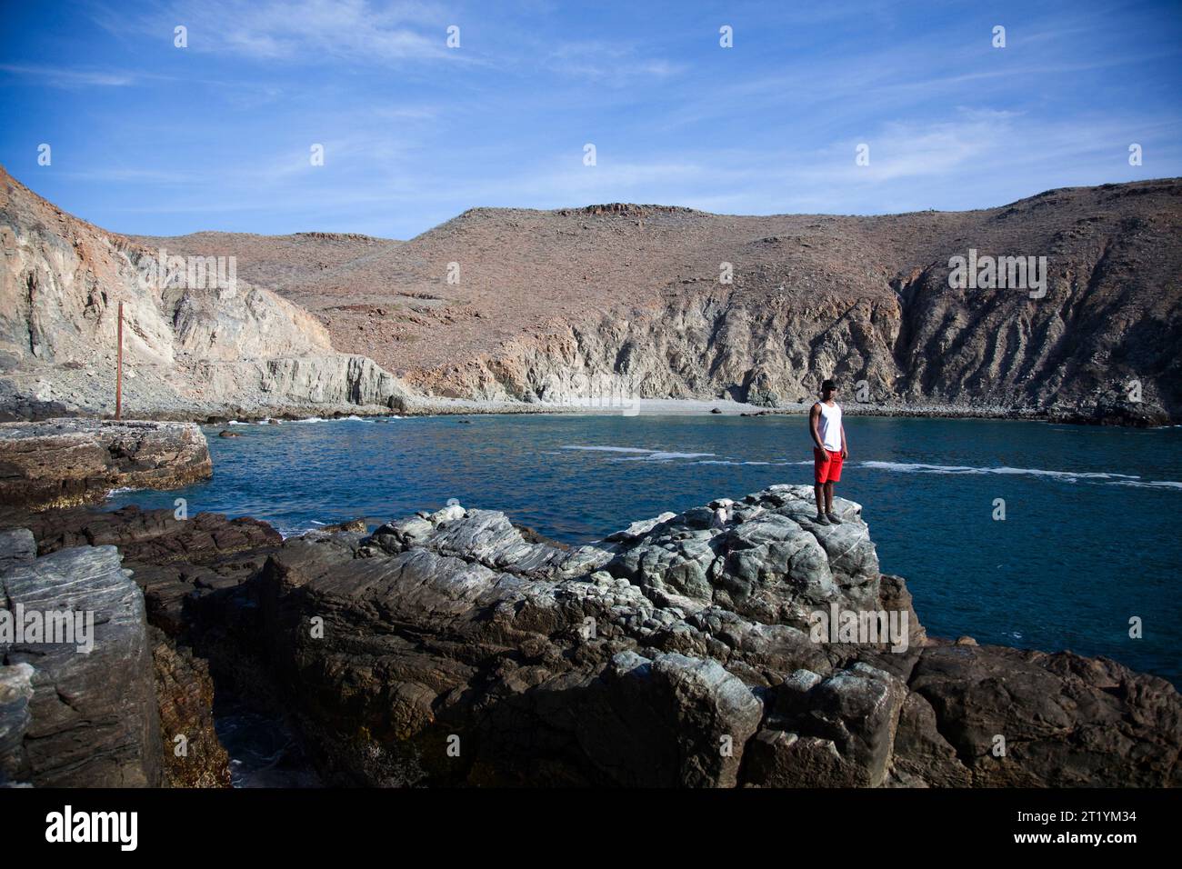 Ein junger Mann steht auf einem Felsvorsprung neben einer kleinen Bucht in der Nähe von Pescadero, Baja California Sur, Mexiko. Stockfoto