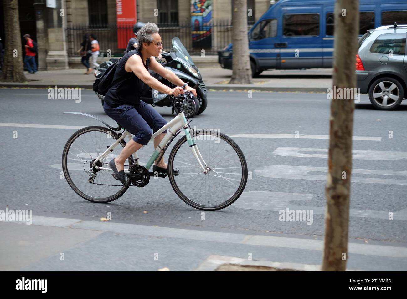 Eine Frau in Singlet und Blau plus vier Hosen, die im abendlichen Verkehr auf dem Boulevard du Palais, Paris, Frankreich, unterwegs ist Stockfoto