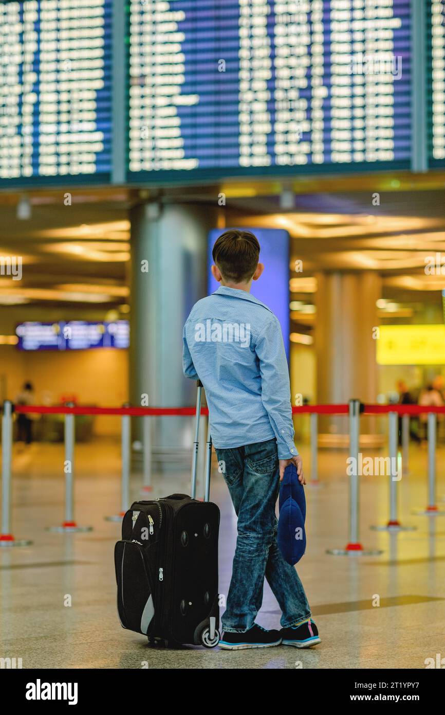 Junge mit einem Koffer vor dem Hintergrund von Zug- oder Flugplänen Stockfoto