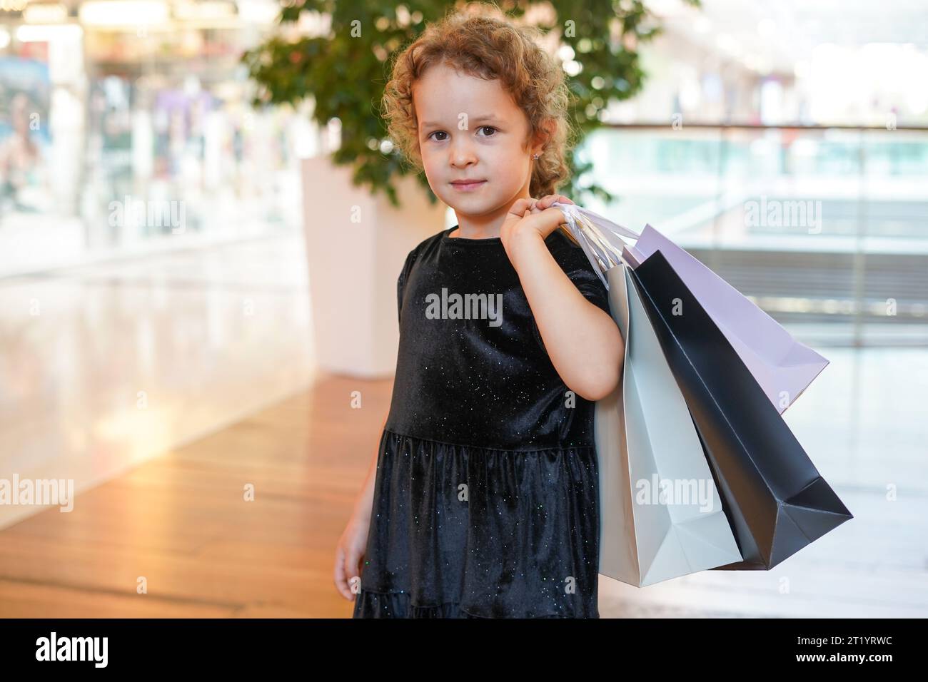 Niedliches Mädchen in schwarzem Kleid beim Einkaufen. Porträt eines Kindes mit Einkaufstaschen. Black Friday-Konzept Stockfoto