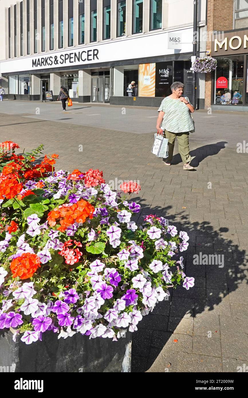 Model veröffentlichte reife Käuferin, die breite Einkaufsmöglichkeiten auf der High Street Straßenbelag bunter Blumenkäufer Marks & Spencer Store Brentwood Essex England spaziert Stockfoto